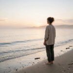 Person standing peacefully on a beach at soft sunrise, for healing quotes